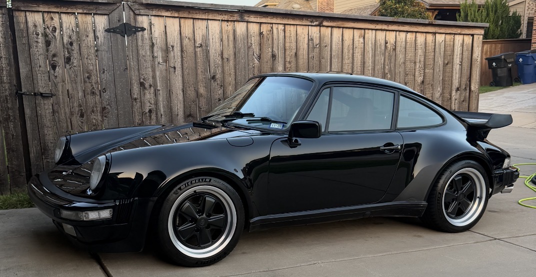 Freshly detailed black Porsche 911 in a driveway at dusk